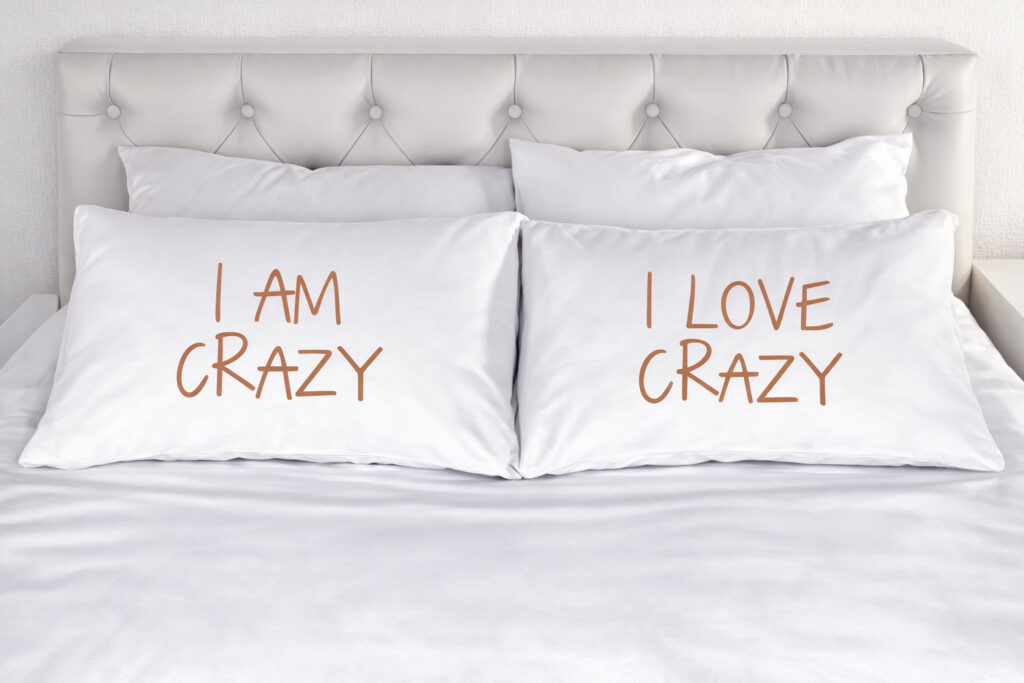 Zwei Kissen auf einem Bett mit der Aufschrift 'I am Crazy' und 'I love Crazy' als Symbol für Akzeptanz und einen sicheren Raum in der Sexualberatung online.