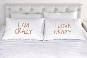 Zwei Kissen auf einem Bett mit der Aufschrift 'I am Crazy' und 'I love Crazy' als Symbol für Akzeptanz und einen sicheren Raum in der Sexualberatung online.